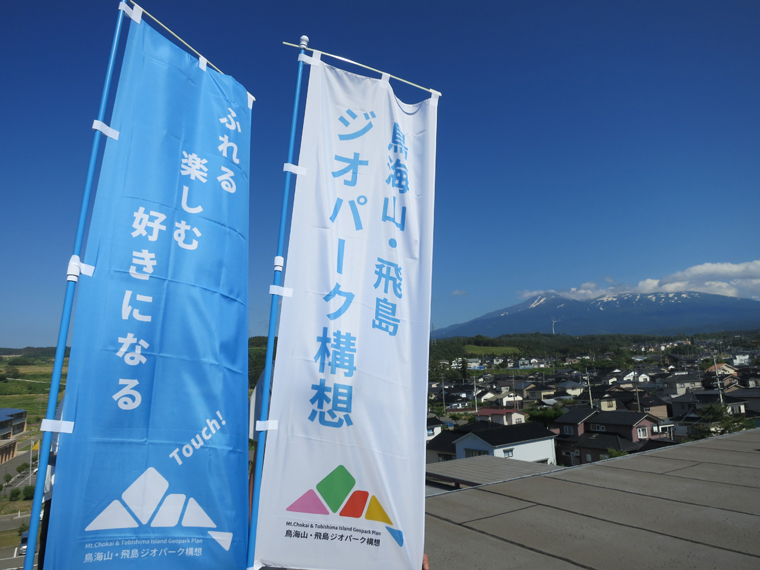 鳥海山・飛島ジオパーク構想のロゴマーク、のぼりと背景には鳥海山の様子