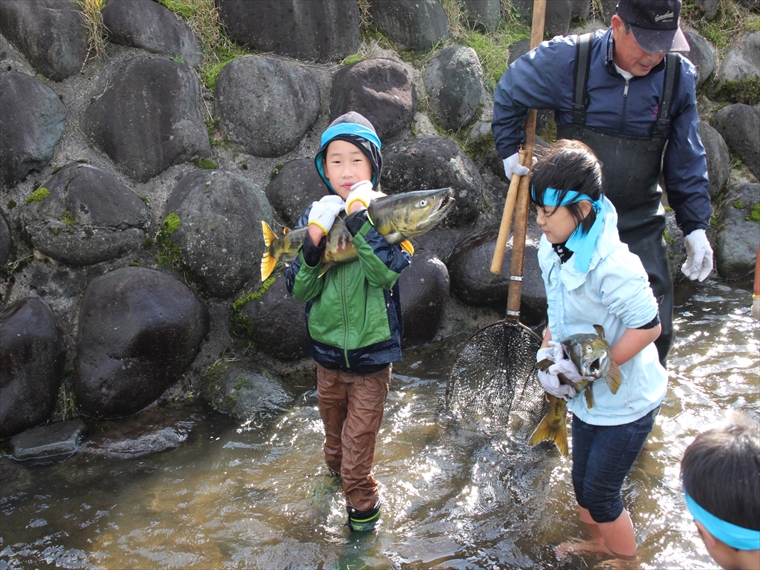 鮭を抱きかかえ、笑顔の子供たちの様子